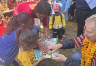 Handing out pencils and writing books to the students.